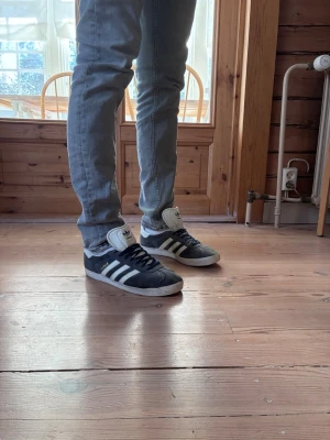 Adidas Originals Gazelle mörkblå - Säljer ett par klassiska Adidas Originals Gazelle sneakers i mörkblå mocka med vita detaljer och de ikoniska tre ränderna på sidan. Skorna har vit plös och sula samt svart snörning. Perfekta för dig som gillar retrostil och streetwear. Skorna är rikligt använda, men har mycket kvar att ge. Skick: 6,5-7/10. 