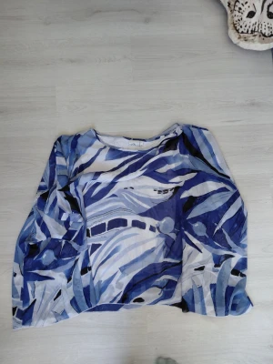 Blåmönstrad blus från Isolde - Säljer en luftig blus från Isolde med abstrakt blått och vitt mönster. Blusen har lång ärm och rund halsringning. Materialet känns lätt och flowy, perfekt för en cool och avslappnad stil.