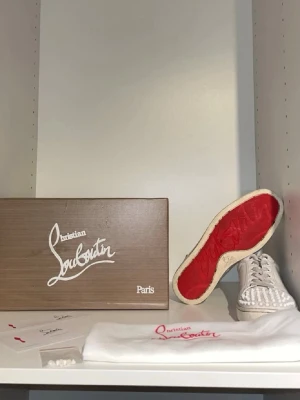 Christian Louboutin vita sneakers med nitar - Säljer ett par vita sneakers från Christian Louboutin med ikoniska röda sulor och coola vita nitar på tån. Skorna har lågt skaft, snörning och är tillverkade i läder. Perfekta för dig som vill sticka ut med en lyxig och edgy stil. Det är äkta och om du har någon fråga eller fundering så är det bara att skriva. Pris går att diskutera.