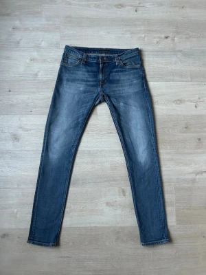 Blåa Nudie Skinny Lin Jeans Storlek W33 L32 - Mycket fina Nudie Jeans i blå färg. Jeansen är i mycket bra skick och sparsamt använda. |  Äkta som allt annat jag säljer! ✅ |  Storlek: W33 L32 | Skick: Mycket Bra Skick - tyvärr en väldigt liten fläck men det är inget som syns (SE SISTA BILD) | Färg: Blå | Märke: Nudie | Modell: Jeans |   Hör gärna av dig vid frågor så svarar jag så fort jag kan! 😁 |  (SKU - 116)
