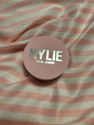Kylie Jenner Setting Powder 100 Translucent - Kylie Jenner Setting Powder i färgen 100 Translucent. Kommer i en rund, ljusrosa burk med silvrig logga. Puderformulan är transparent och passar för att fixera foundation och ge en matt finish. Perfekt för dig som vill ha en naturlig look.