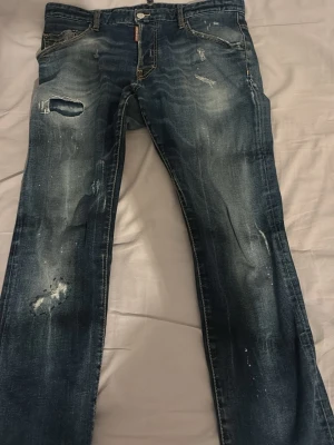 Blå slitna jeans från Dsquared2 - Säljer ett par blå jeans från Dsquared2 med slitningar, hål och distressed detaljer. Jeansen har klassisk femficksmodell, dragkedjegylf och tydliga tvättade partier för en cool look. Perfekta för dig som gillar streetstyle och edgy mode.