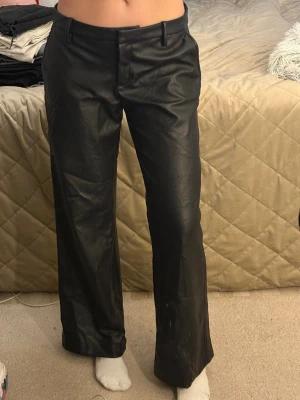 Svarta raka byxor i skinnimitation - Ett par lågmidjade skinnbyxor, raka/vida från HM. Använda fåtal gånger i bra skick, med lite loose fit. Lite korta för mig som är 172-173. 