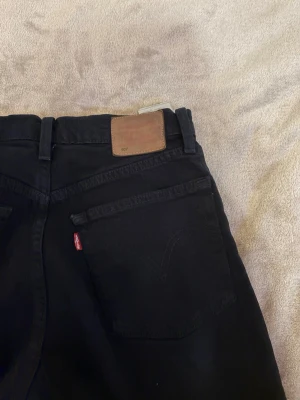 Svarta Levi's jeans med rak passform - Säljer ett par svarta jeans från Levi's med klassisk rak passform och femficksmodell. Jeansen har den ikoniska röda Levi's-lappen på bakfickan och ett brunt läderpatch i midjan. Perfekta till en avslappnad streetwear-look.