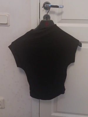Svart croppad topp med kort ärm - En svart, croppad topp med korta ärmar och enkel design. Perfekt för att matcha med höga jeans eller kjol. Toppens material känns mjukt och stretchigt, vilket gör den bekväm att bära hela dagen.