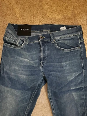 Dondup George - Snygga blå slim fit jeans från Dondup med klassisk femficksdesign och ljusa slitningar framtill. Modell George. Storlek 34. Säljs då jag inte använder de längre. Mitt pris 500kr. Kontakta mig om du har frågor eller vill köpa jeansen.