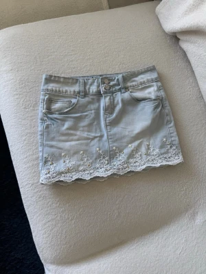 Ljusblå jeanskjol broderi och detaljer - Ljusblå jeanskjol med broderi och detaljer från Blind Date.  Säljer då den tyvärr är lite stor på mig!  Det saknas en nit/pärla på baksidan men inget jag tycker man märker av!  Kika gärna in mina andra plagg, vill få bort så mycket som möjligt 😊