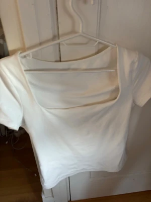 Vit topp med fyrkantig ringning - Snygg vit topp med korta ärmar och trendig fyrkantig ringning. Modellen är croppad och har en clean, minimalistisk look som passar till mycket. Tillverkad i mjukt bomullsmaterial för skön känsla.
