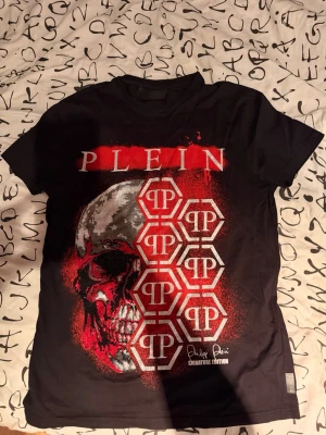 Svart t-shirt från Philipp Plein - Svart t-shirt från Philipp Plein med dödskalletryck säljes i nyskick, då den endast är använd cirka tre gånger. Tröjan är handtvättad för att bevara kvalitet och passform. Nypris var 9 299 kr och den är köpt hos Johnells. Äkthet kan bevisas med utdraget kvitto från Johnells. Tshirten säljs billigt för det inte är min stil längre