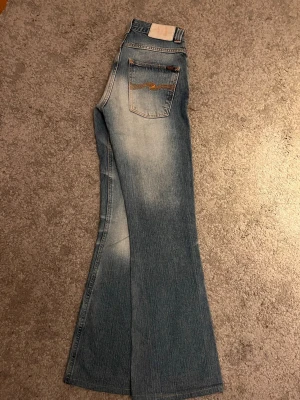 2000s Bootcut Nudie jeans  - Säljer ett par ljusblåa bootcut Nudie Jeans av modellen "Flare Jan" från tidigt 2000-tal (2001-2005), designade av Maria Erixon (Nudies grundare) när produktionen fortfarande vad baserad i Italien. Jeans för jeansnördar eller någon som vill vara stylish som fan. Ett plagg som tillhör modehistoria. Slitningar och ljusa partier fram- och baktill. Y2K vågens mamma.                                                   Midjemått: 68cm, Innerbenslängd: 80cm        W27 L31