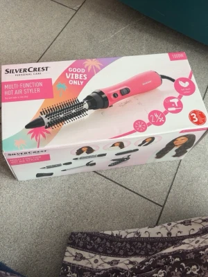 SilverCrest multifunktionell varmluftsborste - Multifunktionell varmluftsborste från SilverCrest i rosa plast med flera utbytbara tillbehör för styling av håret. Perfekt för att skapa volym, lockar eller släta längder. 1000W effekt och ergonomiskt handtag. Levereras i originalförpackning.