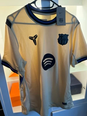 FC Barcelona gul matchtröja Nike - Snygg gul FC Barcelona matchtröja från Nike med blå detaljer och klubbmärke på bröstet. Tröjan har korta ärmar, rund hals och är tillverkad i lätt, ventilerande Dri-FIT-material. Perfekt för fotbollsträning eller att bära som supporter.