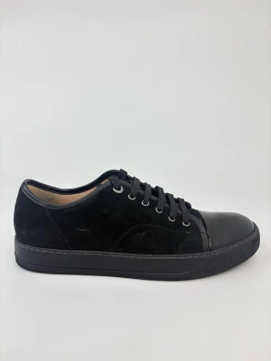Svarta Lanvin sneakers med lackad tå - Stilrena svarta sneakers med ovandel i mocka och snygg lackad tå i svart. Skorna har svarta skosnören, metallfärgade öljetter och en klassisk låg siluett. Perfekta för dig som gillar en clean look med en twist. Yttersulan är också svart för en helsvart vibe.