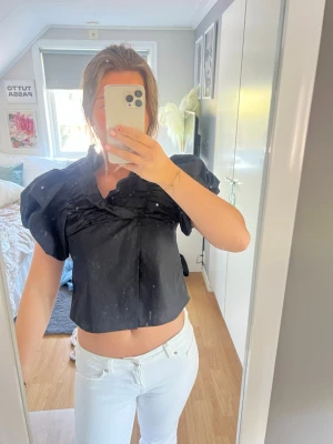 Svart blus med puffärmar - Snygg svart blus med korta puffärmar och veckade detaljer framtill. Modellen är croppad och har en lös passform. Bara använd en gång under 3 timmar. 