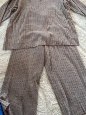 Beigeset ribbat loungewear-set - Mysigt loungewear-set i beige med ribbad struktur. Setet består av en långärmad tröja och matchande byxor med resår i midjan. Perfekt för chill dagar hemma. Materialet känns mjukt och stretchigt, vilket gör det superbekvämt.