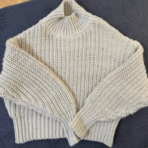 Beige stickad polotröja - Säljer en beige stickad polotröja med breda ärmar och ribbade muddar. Tröjan har en hög krage och är gjord i ett tjockt, mjukt garn som ger en chunky känsla. Perfekt för kalla dagar och enkel att styla till olika outfits.