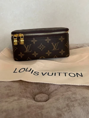 Monogram necessär - Säljer en exklusiv necessär från Louis Vuitton i klassiskt brunt monogrammönster med guldiga dragkedjor. Väskan är rektangulär och tillverkad i slitstarkt canvasmaterial med LV-logga och detaljer i läder. Perfekt för att förvara småsaker eller smink.