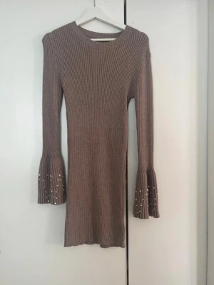 ribbad stickad klänning - Snygg beige stickad klänning med ribbad struktur och utsvängda ärmar dekorerade med pärlor. Klänningen har lång ärm och är i kort modell.