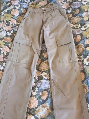 Beige cargobyxor med stora fickor - Säljer ett par beige cargobyxor med raka ben och stora fickor på sidorna. De har en liten missfärgning vid en av fickorna på benet, inget som syns jättetydligt men därav priset. Pris går ändå som vanligt att diskutera 💞  