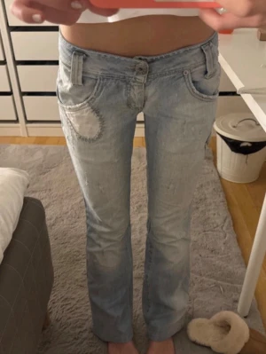 Ljusblå bootcut jeans - Säljer ett par ljusblå bootcut jeans med låg midja och en cool vit patchdetalj på ena fickan. Jeansen har en låg midja och Bootcut och klassisk femficksmodell. Perfekta för en avslappnad och trendig look. Midjemåttet är 33 cm och innerbenslängden är 79❤️❤️ jag är 167