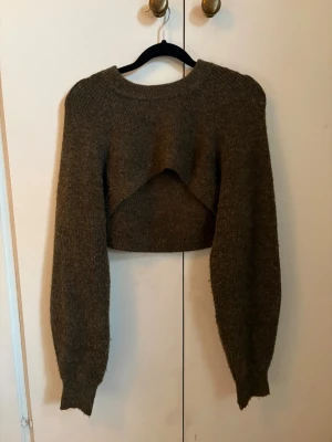 Mörkgrön croppad stickad tröja - Säljer en mörkgrön bolero med rund halsringning och långa, puffiga ärmar. Tröjan är gjord i ett mjukt, tjockt material som passar perfekt till lager på lager. 