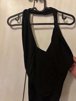 Svart halterneck baddräkt - Enkel och stilren svart topp med halterneck och djup urringning. Toppen har breda axelband och öppen rygg, vilket ger en modern och smickrande siluett. Aldrig använd, prislapp kvar. 