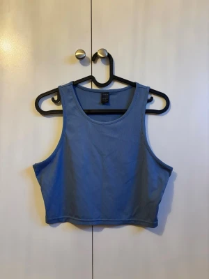 Blå ribbad croppad linnetopp - Säljer en blå croppad linnetopp med ribbad struktur. Toppen är ärmlös och har en rund halsringning, perfekt för varma dagar eller som layering-piece. Enkel och stilren design som passar till det mesta.