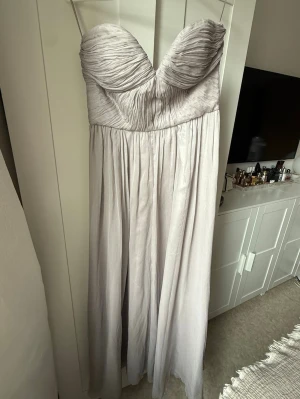 Grå maxiklänning - Snygg grå maxiklänning med draperad byst och axelbandslös design. Klänningen har plisserat fall och markerad midja. Perfekt för bal och bröllop, passar mig som är 165cm och har storlek s/m. Använd en gång.