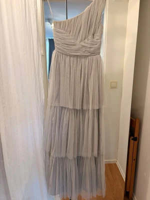 Ljusgrå balklänning med volanger  - Säljer min balklänning. Den är ljusgrå med volanger och oneshoulder. Klänningen har draperingar upptill och en volangkjol. I storlek 36 men lång. Köpt på ASOS.  Jätte bra skick och otroligt fin. 👗🌸❤️