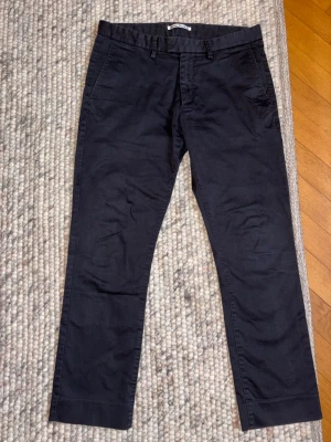 Svarta chinos från Acne Studios - Snygga svarta chinos från Acne Studios med klassisk rak passform och bälteshällor. Byxorna har två sidofickor fram och två bakfickor, varav en med knapp. Tillverkade i ett mjukt bomullstyg som ger en skön känsla hela dagen.