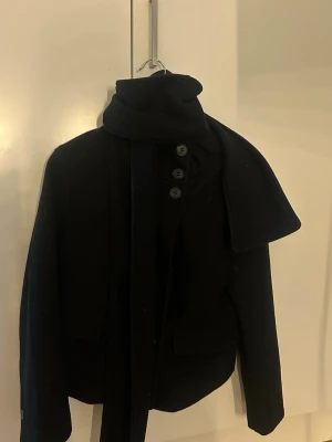 Svart kappa  - En vår kappa med en halsduk insydd. Väldigt läcker på! Knapparna går upp till halsen så man är varm. 