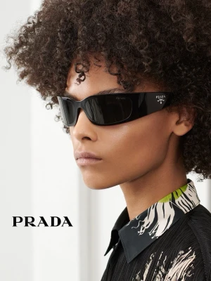Svarta solglasögon från Prada - Snygga svarta solglasögon från Prada med breda skalmar och vit logga på sidan. Glasögonen har en modern, kantig form och är tillverkade i ett tåligt syntetmaterial. Perfekta för dig som vill ha en stilren och exklusiv look.