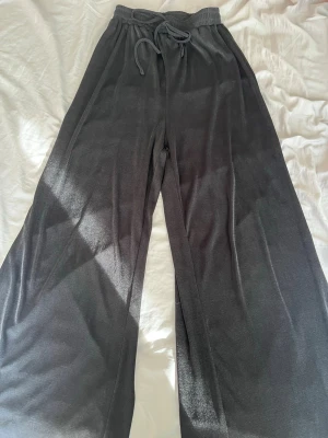 Svarta vida mjukisbyxor - Säljer ett par svarta mjukisbyxor med breda ben och resår i midjan samt dragsko. Byxorna är tillverkade i ett mjukt och skönt material som känns riktigt bekvämt. Perfekta för chill dagar hemma eller när du vill ha en avslappnad stil.