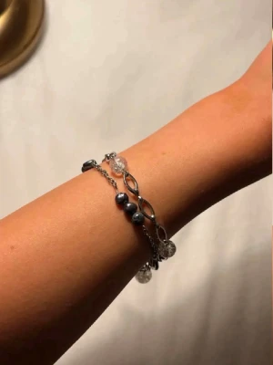 Silverfärgat armband med pärlor - Snyggt armband i silverfärg med kedja och dekorativa detaljer. Armbandet har svarta och genomskinliga pärlor samt tvinnade länkar som ger en cool och trendig look. Perfekt accessoar för att lyfta din outfit.