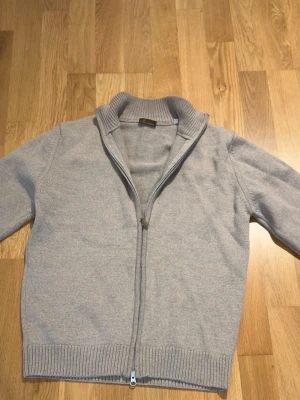 Ljus Beige ziptröja med hög krage - Snygg ljusgrå ziptröja med hög ribbad krage och dragkedja hela vägen. Tröjan har långa ärmar och ribbade muddar vid ärmslut och nederkant. Perfekt för lager på lager och enkel att matcha med olika outfits. Ny pris ca 3000kr pris kan diskuteras.