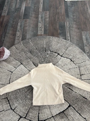 Beige ribbad polotröja - Snygg beige stickad polotröja med ribbad struktur. Tröjan har långa ärmar och en hög krage som ger en stilren look. Perfekt att matcha med jeans eller kjol för en trendig outfit.