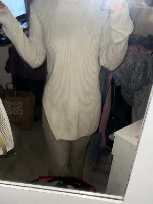 Beige ribbstickad polotröja - Säljer en beige ribbstickad polotröja med lång ärm och hög krage. Tröjan är längre i modellen och har slits på sidan för en snygg och avslappnad look. Perfekt att styla med leggings eller jeans.