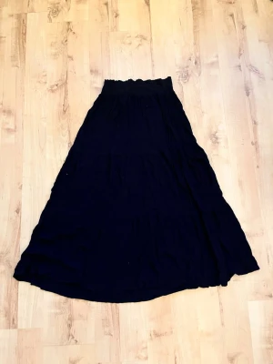 Svart långkjol från 157 - Säljer en svart långkjol från 157 med smockad midja för skön passform. Kjolen har en vid och flowy siluett som ger en avslappnad look. Tillverkad i mjukt tyg som känns bekvämt mot huden. Perfekt att styla med crop top eller stickad tröja.