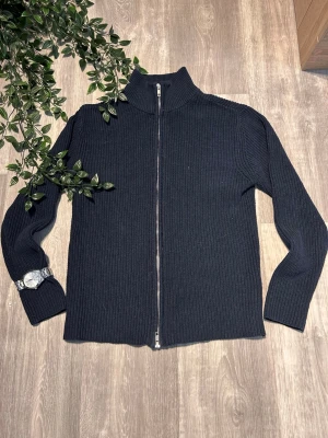 Mörkblå stickad ziptröja - Mörkblå stickad tröja med hel dragkedja framtill och hög krage. Tröjan har lång ärm och är ribbstickad för en snygg struktur. Perfekt för lager på lager och enkel att matcha med olika outfits.