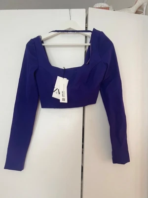 Lila croppad topp från Zara - Trendig lila croppad topp från Zara med fyrkantig ringning och långa ärmar. Toppen har en stilren och modern look som passar perfekt till höga jeans eller kjol. Materialet känns mjukt och följsamt mot kroppen.