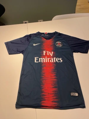 PSG Neymar Jr matchtröja blå - Säljer en blå Paris Saint-Germain matchtröja från Nike med Neymar Jr och nummer 10 på ryggen. Tröjan har röd och vit detalj framtill, Fly Emirates-tryck och PSG-logga på bröstet. Tillverkad i lätt och ventilerande material, perfekt för fotbollsträning.
