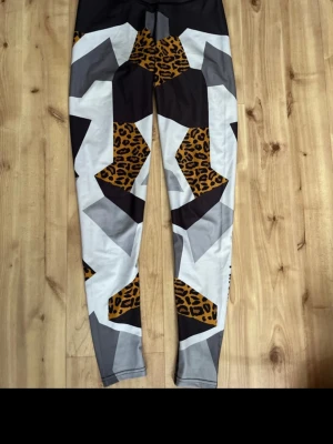 Mönstrade leggings från ICANIWILL - Snygga leggings från ICANIWILL med coolt grafiskt mönster i svart, vitt, grått och leopardmönstrade detaljer i gult och brunt. Hög midja med logotyp i midjebandet. Stretchigt material som passar perfekt till träning eller gym.