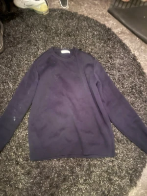 Mörkblå stickad tröja unisex - En enkel och stilren mörkblå stickad tröja med rund halsringning och långa ärmar. Tröjan har ribbade muddar vid ärmslut och nederkant. Perfekt att matcha med jeans eller kjol för en avslappnad look.