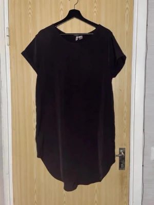 Svart t-shirtklänning från H&M Divided - Enkel svart t-shirtklänning från H&M Divided i storlek 42. Klänningen har rund halsringning, korta ärmar och rak passform. Perfekt basplagg som är lätt att styla med accessoarer eller sneakers.