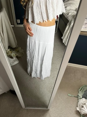 Vit långkjol i bomull - Säljer en enkel och flowy vit långkjol i mjuk bomull. Kjolen har en rak passform och faller snyggt längs benen, perfekt till sommaren. Inga synliga detaljer eller mönster, bara clean och stilren look.