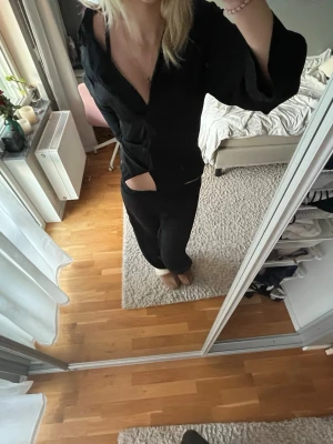 Svart pyjamas-set med skjorta - Säljer ett svart pyjamas-set med långärmad skjorta och matchande byxor. Skjortan har knappar framtill och en avslappnad passform. Materialet ser mjukt och bekvämt ut, perfekt för hemmamys. Klassisk och stilren design.