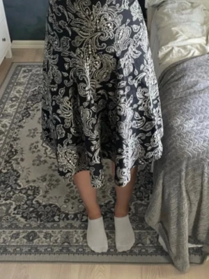 Svart axelbandslös klänning med mönster - Säljer en svart axelbandslös klänning med vitt paisley-inspirerat mönster. Klänningen har en vid kjol 