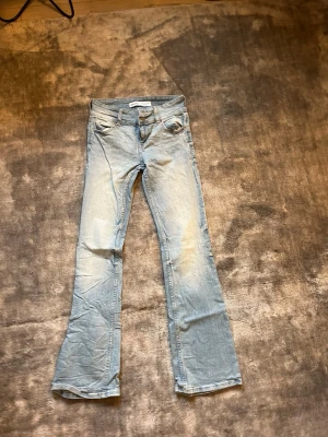 Ljusblå bootcut jeans - Säljer ett par ljusblå bootcut jeans med klassisk femficksdesign och låg midja. Jeansen har en snygg tvättad look och är tillverkade i ett mjukt denimtyg som ger en avslappnad vibe. 