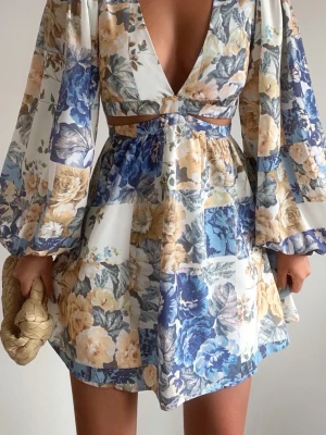Blommig kortklänning med cut-outs - Superfin kortklänning med blommigt mönster i blått, beige och vitt. Djup v-ringning, vida långärmar och trendiga cut-outs vid midjan. Klänningen har en flowy passform och är gjord i ett lätt, luftigt material som passar perfekt till sommaren. Helt ny lappar kvar 🌸Storlek 36