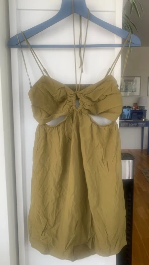 Olivgrön kort klänning med cut-out - Trendig olivgrön kort klänning från H&M med smala axelband och snygga cut-out detaljer framtill och baktill. Klänningen har en rynkad byst och knytband i nacken för en cool och modern look. Perfekt för varma dagar och sommarens alla tillfällen.